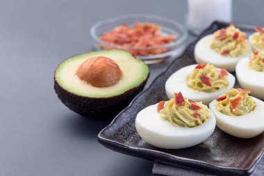 Avokado, yumurta sarısı ve mayonez ile doldurulmuş yumurtalar pastırmayla süslenmiş, yatay, kopya alanı.