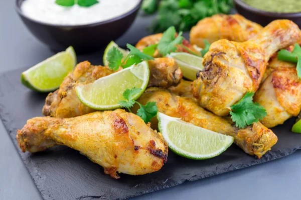 Indian chicken tandoori, marinated in greek yogurt  and spices, served with lime wedges and cilantro on a slate plate, horizontal