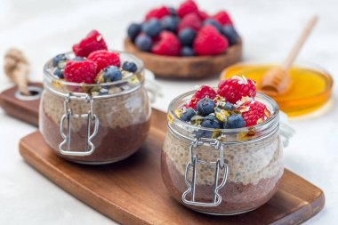 Kavanozda çikolata ve fıstık ezmeli chia tohumu pudingi, ahududu, yabanmersini, bal ve hindistan cevizi taneleriyle süslenmiş, yatay