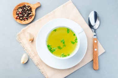 Beyaz bir fincanda ev yapımı tavuk çorbası doğranmış maydanozla süslenmiş, yatay ve üst manzaralı.