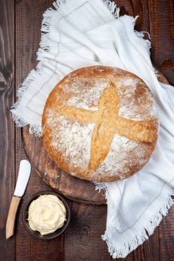 Klasik Boule ekmeğinin yuvarlak somunu tereyağı ile servis edilir, koyu ahşap tahta beyaz kumaşlı, dikey, üst manzaralı. 