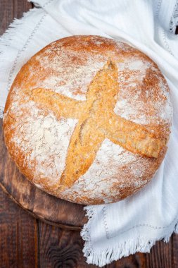 Klasik Boule ekmeğinin yuvarlak somunu, koyu ahşap bir tahtanın üzerinde, beyaz bir bez üzerinde, dikey, üst manzara, yakın çekim 