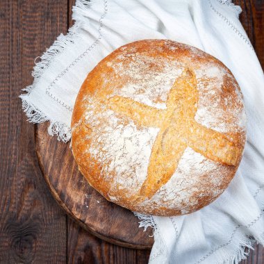 Bir somun klasik Boule ekmeği koyu ahşap tahta üzerinde beyaz kumaş, üst manzara, kare format