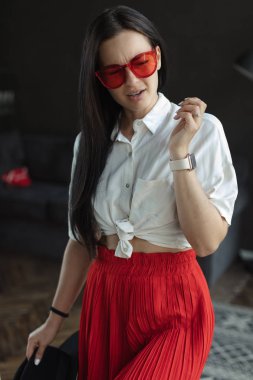 geniş bacaklar ve beyaz gömlek ile kırmızı moda tava muhteşem esmer kadın. ayakkabı olmadan kanepede siyah saçlı moda genç kadın kapalı. rahat ev konsepti. güzel sanatlar kadın portre