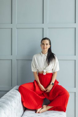 geniş bacaklar ve beyaz gömlek ile kırmızı moda tava muhteşem esmer kadın. ayakkabı olmadan kanepede siyah saçlı moda genç kadın kapalı. rahat ev konsepti. güzel sanatlar kadın portre
