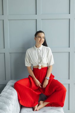 geniş bacaklar ve beyaz gömlek ile kırmızı moda tava muhteşem esmer kadın. ayakkabı olmadan kanepede siyah saçlı moda genç kadın kapalı. rahat ev konsepti. güzel sanatlar kadın portre