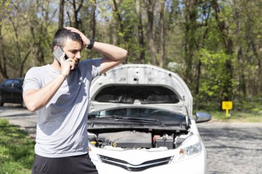 Young man in front of broken down car on the road, calling for HELP clipart