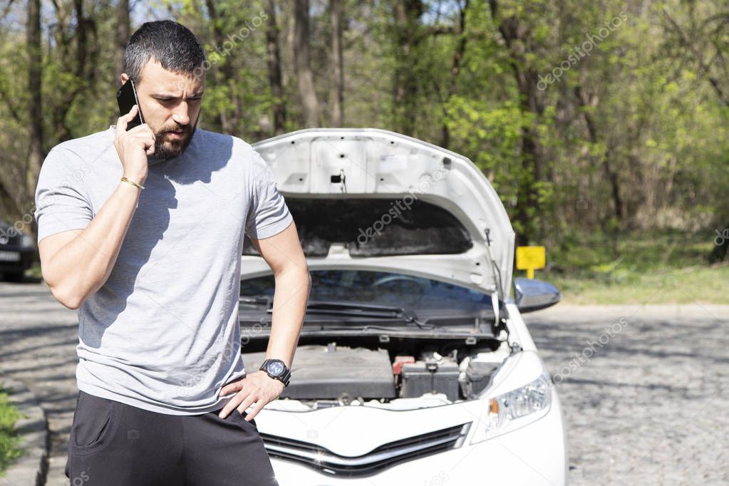 Young man in front of broken down car on the road, calling for HELP