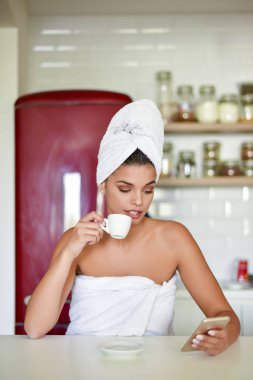 Sabah kahvesi içen ve elinde cep telefonu olan bir kadın.