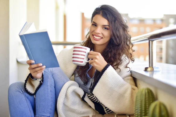 Young woman reads a book and drinks tea at balcony