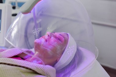 Yüz için renk ışığı terapisi alan kadın. Yüz terapisi. Anti-aging prosedürleri.