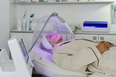 Yüz için renk ışığı terapisi alan kadın. Yüz terapisi. Anti-aging prosedürleri.