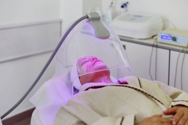 Yüz için renk ışığı terapisi alan kadın. Yüz terapisi. Anti-aging prosedürleri.