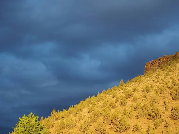 A beautiful golden glow bathes a local butte in Prineville in Central Oregon right after a spring storm with the sky still a stormy dark gray.