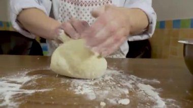 Kapat - eller evdeki masada hamuru yoğur. Elleri mutfakta hamuru hazırlayan bir kadının yakın çekimi.