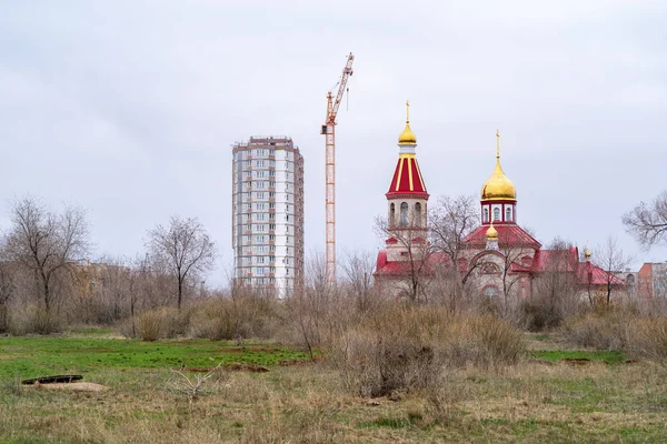 生い茂った荒れ地の教会 ロシア オレンブルク 2019年4月14日 アルタイ通りの正教会とタワークレーンを背景に建設中の高層ビル — ストック写真