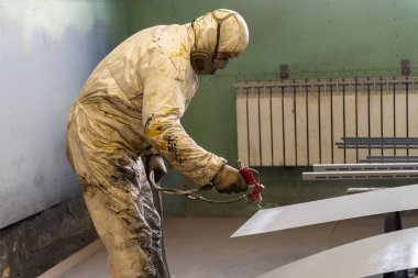Koruyucu tulumlu ressam sprey tabancayla çalışıyor. Fotoğraf fabrika katında çekildi.