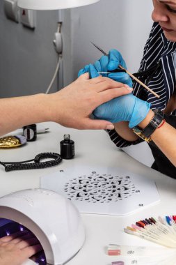 Manikür salonu. Mavi koruyucu eldivenli usta bir fırçayla çalışıyor.