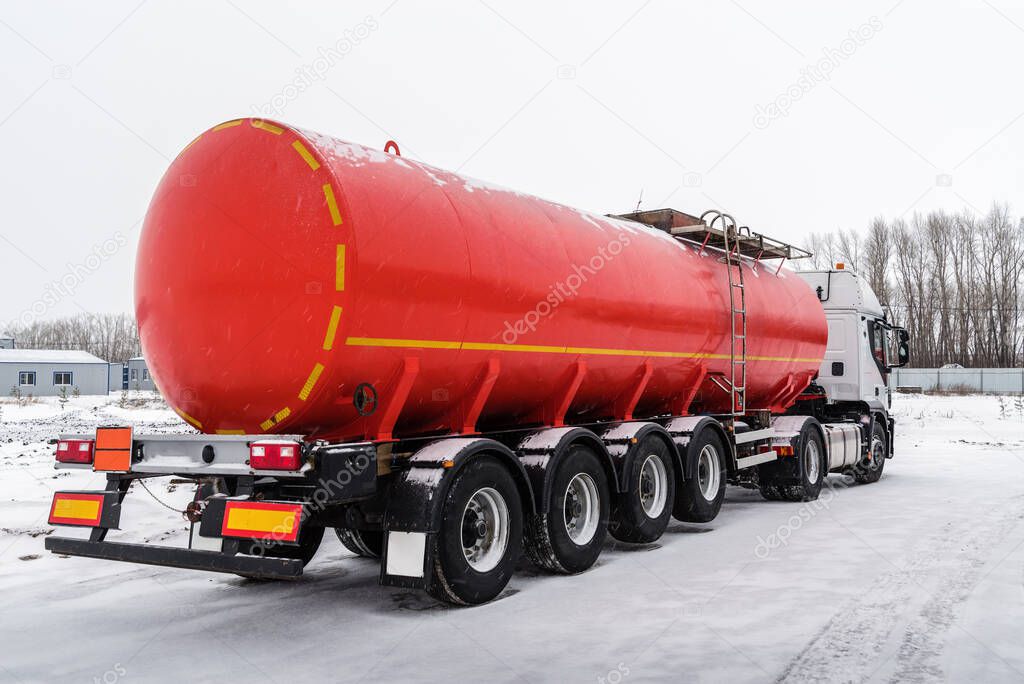 Oil tanker truck with a red tank semi-trailer. The picture was taken in Russia, in winter in snowfall