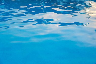 Yüzme havuzunda berrak mavi su yüzeyi güneş ışığını yansıtıyor, sakin ve ferahlatıcı bir yaz manzarası yaratıyor..