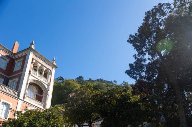Sintra, Portekiz 'de tarihi mimari. Süslü balkonları ve detaylı taş işçiliği olan güzel bir bina ağaçlar tarafından çerçevelenmiştir. Sintra 'nın gür tepeleri ve berrak mavi gökyüzünün altında Moors Kalesi görülebilir..