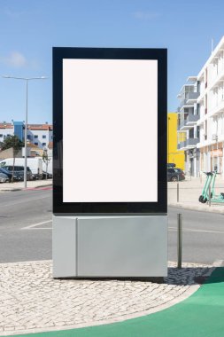 Portekiz 'de bir şehir caddesinde modern boş ilan panosu. Reklam paneli kaldırımda duruyor. Arkasında binalar, arabalar ve elektrikli scooterlar var. Açık mavi bir gökyüzünün altında..
