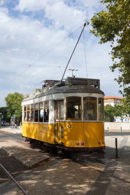 Classic yellow tram on route 24E in Lisbon, Portugal, standing at a stop under a partly cloudy sky.