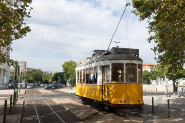 Classic yellow tram on route 24E in Lisbon, Portugal, standing at a stop under a partly cloudy sky.