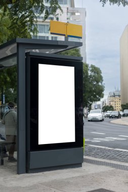 Bus stop with a large blank advertising billboard on a busy avenue, surrounded by tall modern buildings and people waiting inside the shelter. Lisbon Portugal