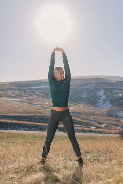 Egzersiz ve güneşli bir günde bir dağın tepesinde germe kadın genç yerleştirmek