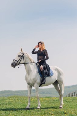 Beyaz atı açık havada siyah elbiseli genç bir kadın.