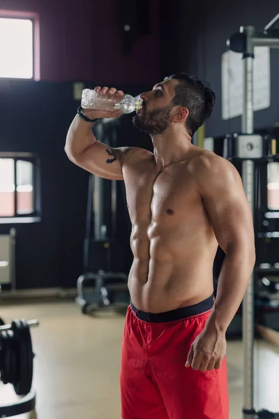 Strong man in the gym drinking water — Stock Photo, Image