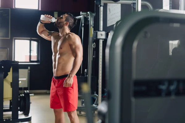 Strong man in the gym drinking water — Stock Photo, Image