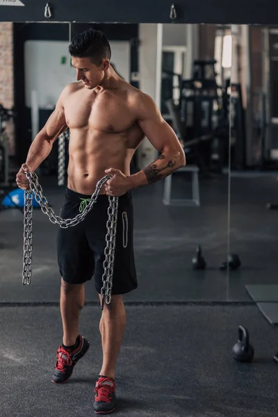 Spor salonundaki genç kaslı adam egzersiz yapıyor.