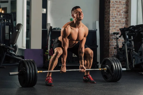 Spor salonundaki genç kaslı adam egzersiz yapıyor.