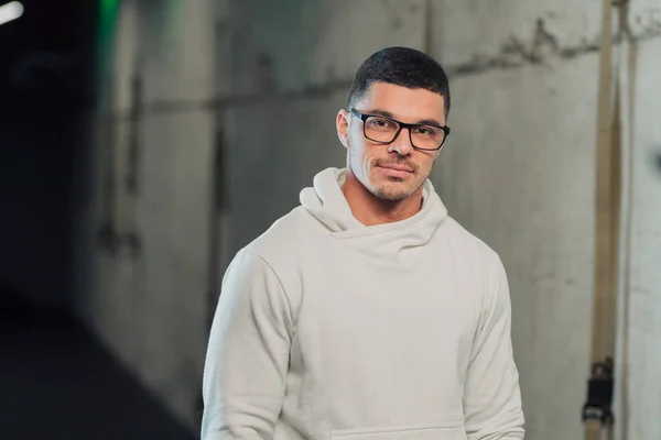 Young strong man in glasses in gym in white hoodie