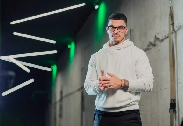 Young strong man in glasses in gym in white hoodie