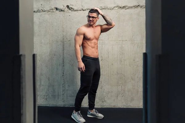 Beton duvarın yanında gözlüklü güçlü genç adam.
