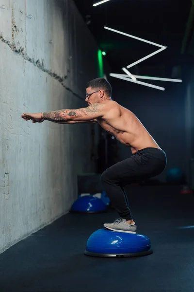 Jimnastik salonundaki genç güçlü adam spor salonunda çömeliyor.