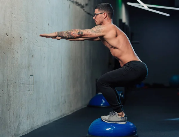 Jimnastik salonundaki genç güçlü adam spor salonunda çömeliyor.