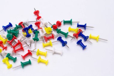Kırmızı, mavi, yeşil, sarı ve beyaz renkli itme iğnelerinden oluşan dağınık bir koleksiyon, temiz beyaz arka planda sergilenmektedir..