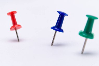 Kırmızı, mavi ve yeşil renklerde, temiz beyaz bir yüzey üzerinde dik duran üç itme iğnesinin yakın çekim görüntüsü..
