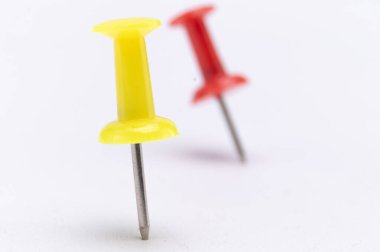 Arkasında bulanık bir pim olan sarı itme iğnesinin yakın çekim görüntüsü, temiz beyaz bir arkaplan üzerine kurulmuş..