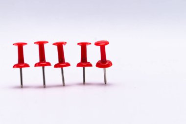 Beş kırmızı raptiye, temiz ve beyaz bir yüzeyde düz bir çizgide sıralanır. İğneler eşit aralıklarla ve ince gölgeler halinde..