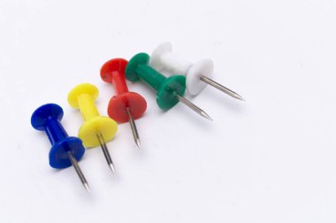 Mavi, sarı, kırmızı, yeşil ve beyaz beş itme iğnesi yakın plan temiz beyaz bir yüzey üzerinde çapraz dizilmiş.