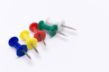 Mavi, sarı, kırmızı, yeşil ve beyaz beş itme iğnesinin yakın çekim görüntüsü, temiz beyaz bir yüzey üzerinde çapraz dizilmiş..