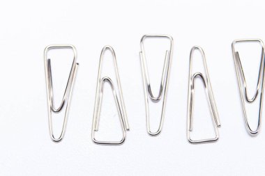 Beyaz arka planda beş gümüş ataç, ofis malzemesi ve kırtasiye malzemesi sergileniyor..