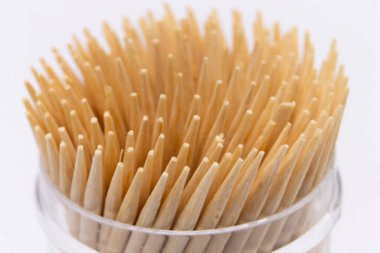 Yüksek açılı, yakın plan bir sürü tahta kürdan, temiz bir plastik kabın içinde bir araya toplanmış, düz beyaz arka plan üzerine kurulmuş.