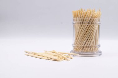 Tahta kürdanlarla dolu şeffaf plastik bir kap temiz, beyaz bir yüzey üzerinde dağınık kürdanların yanında duruyor..