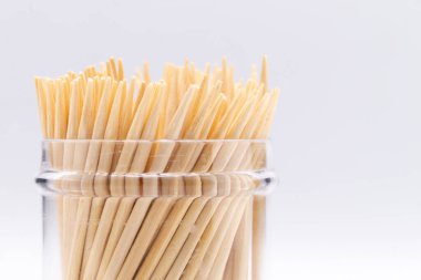 Temiz, beyaz bir zemin üzerine kurulmuş, tahta kürdanlarla dolu cam bir kabın yakın plan çekimi. Kürdanların dokusu ve düzenine odaklan.